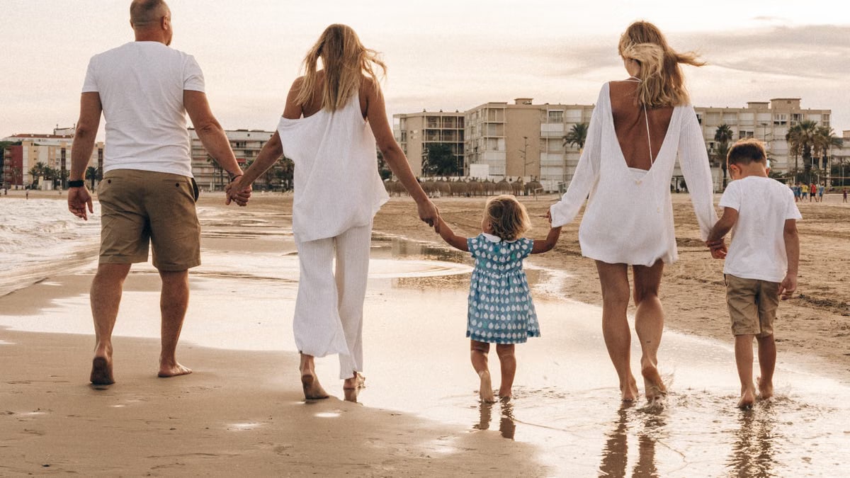Family walking hand in hand along the beach at sunset, enjoying a warm summer day.